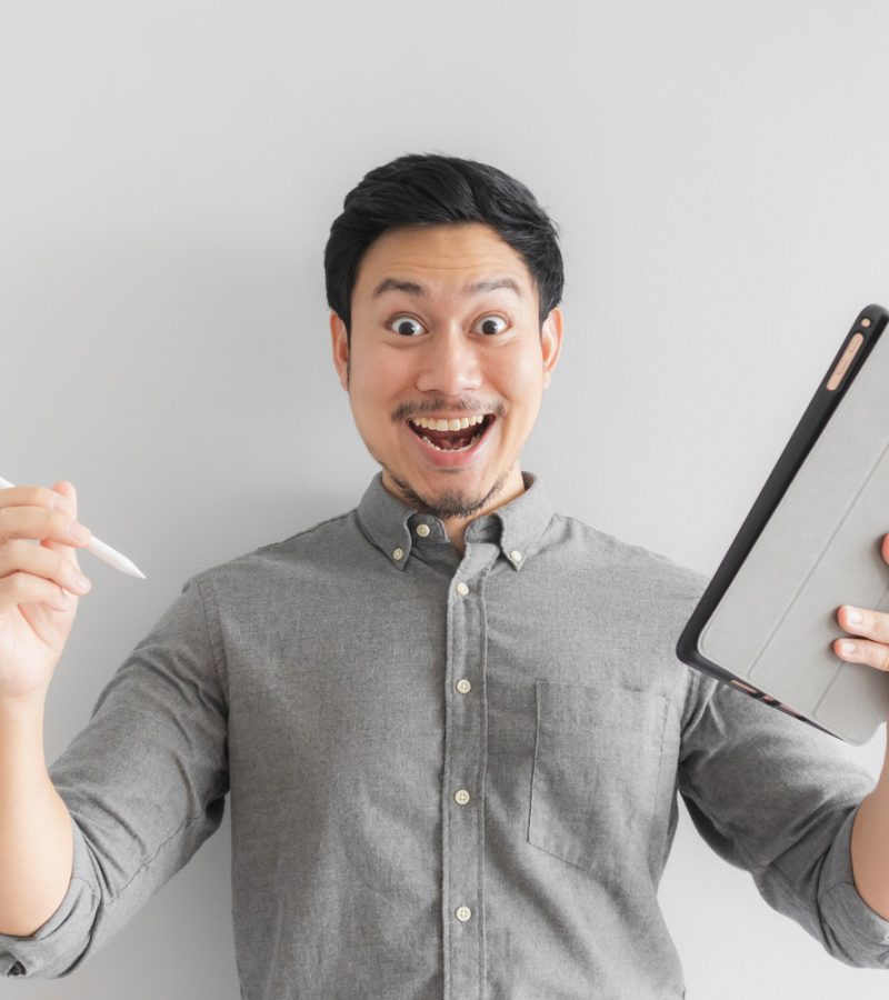 Wow and surprised Asian entrepreneur businessman work on his tablet with grey background.